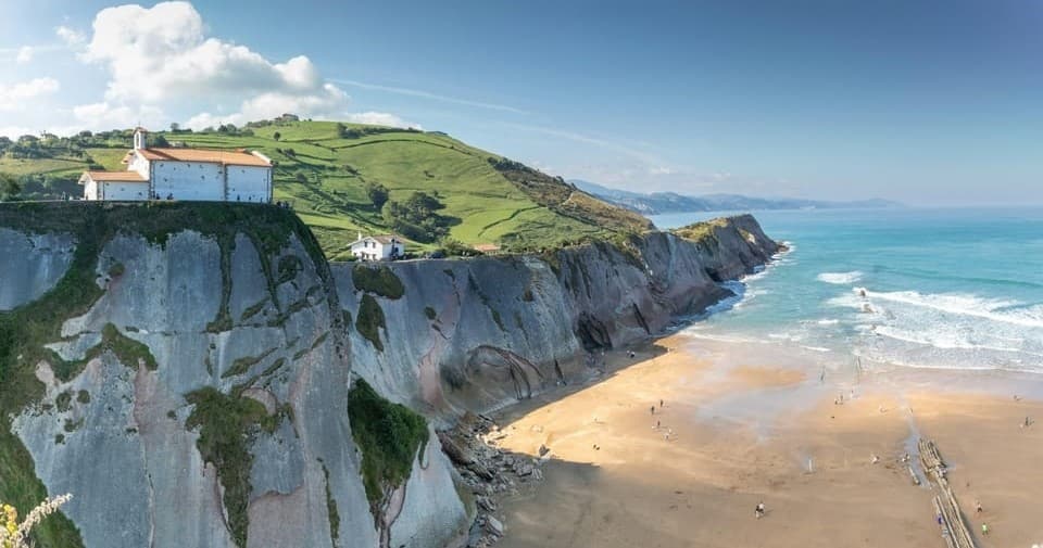 Sunlit coastal cliffs overlooking sandy beach and surfers