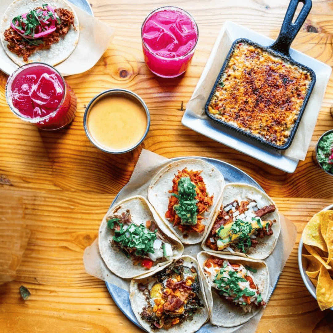 Overhead plate of tacos and drinks on wooden table for tasting