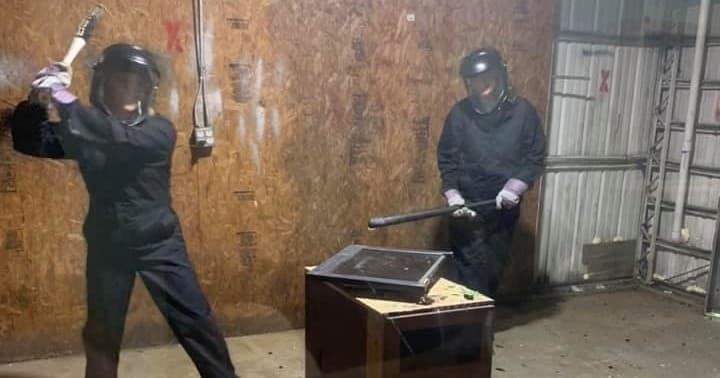 Two participants swinging sledgehammers in indoor rage room
