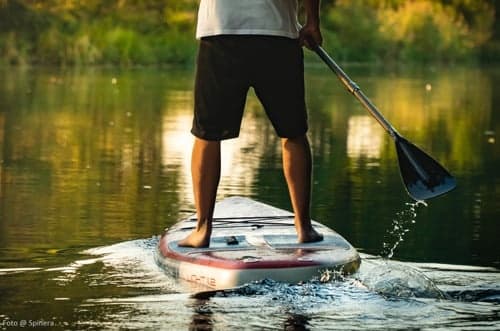 Stand-up paddleboarder paddling on reflective river at dusk