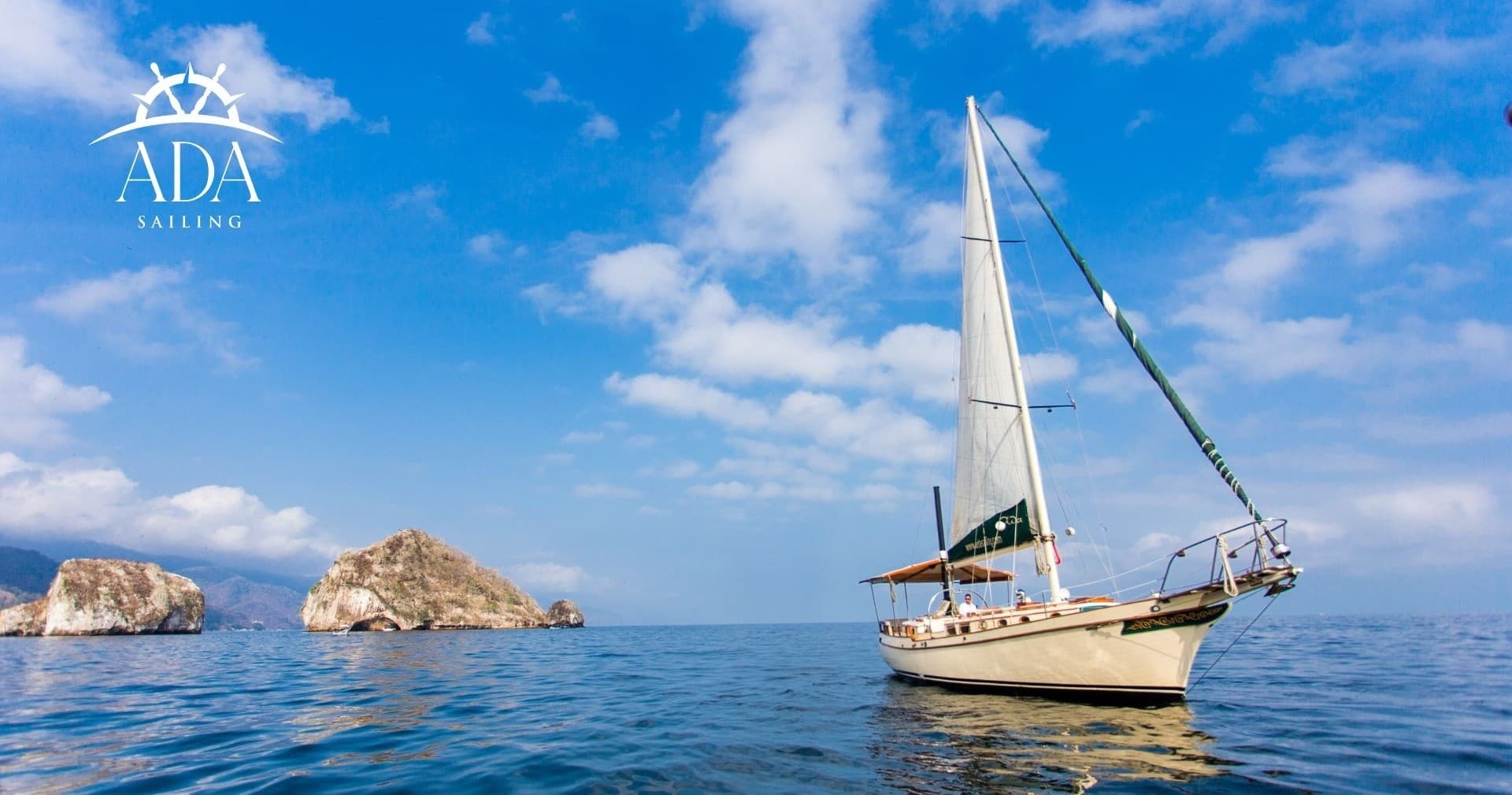 Sailboat gliding near rocky islets under bright blue sky