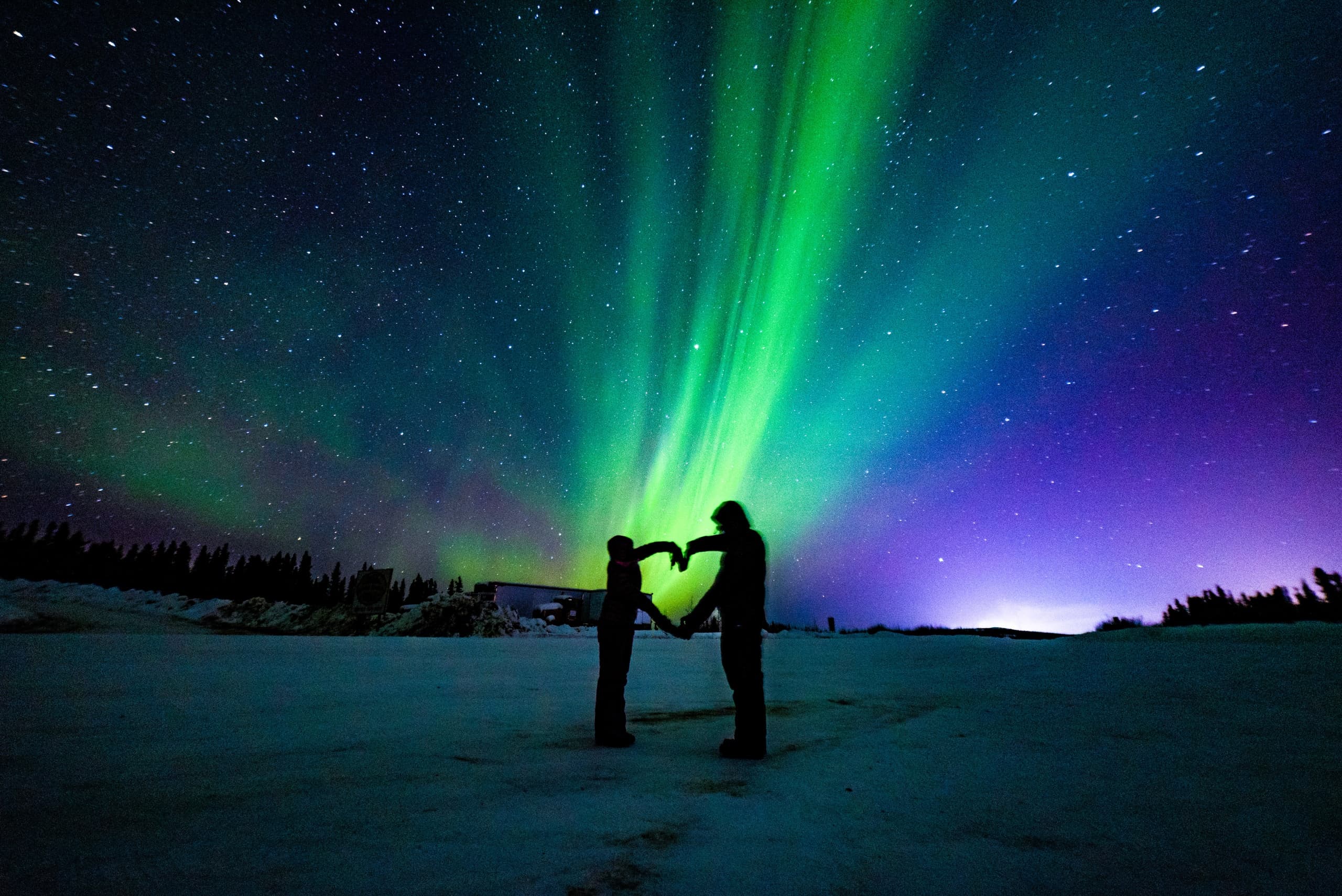 Couple forming heart under vibrant northern lights on tundra