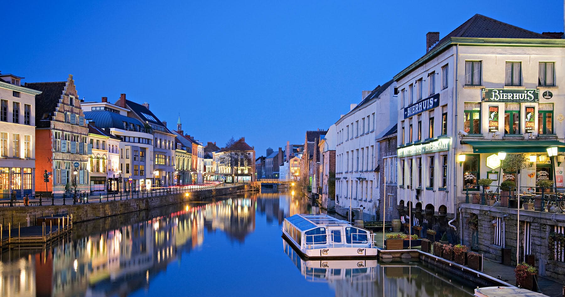 Scenic Belgian canal at dusk with boats and riverside buildings