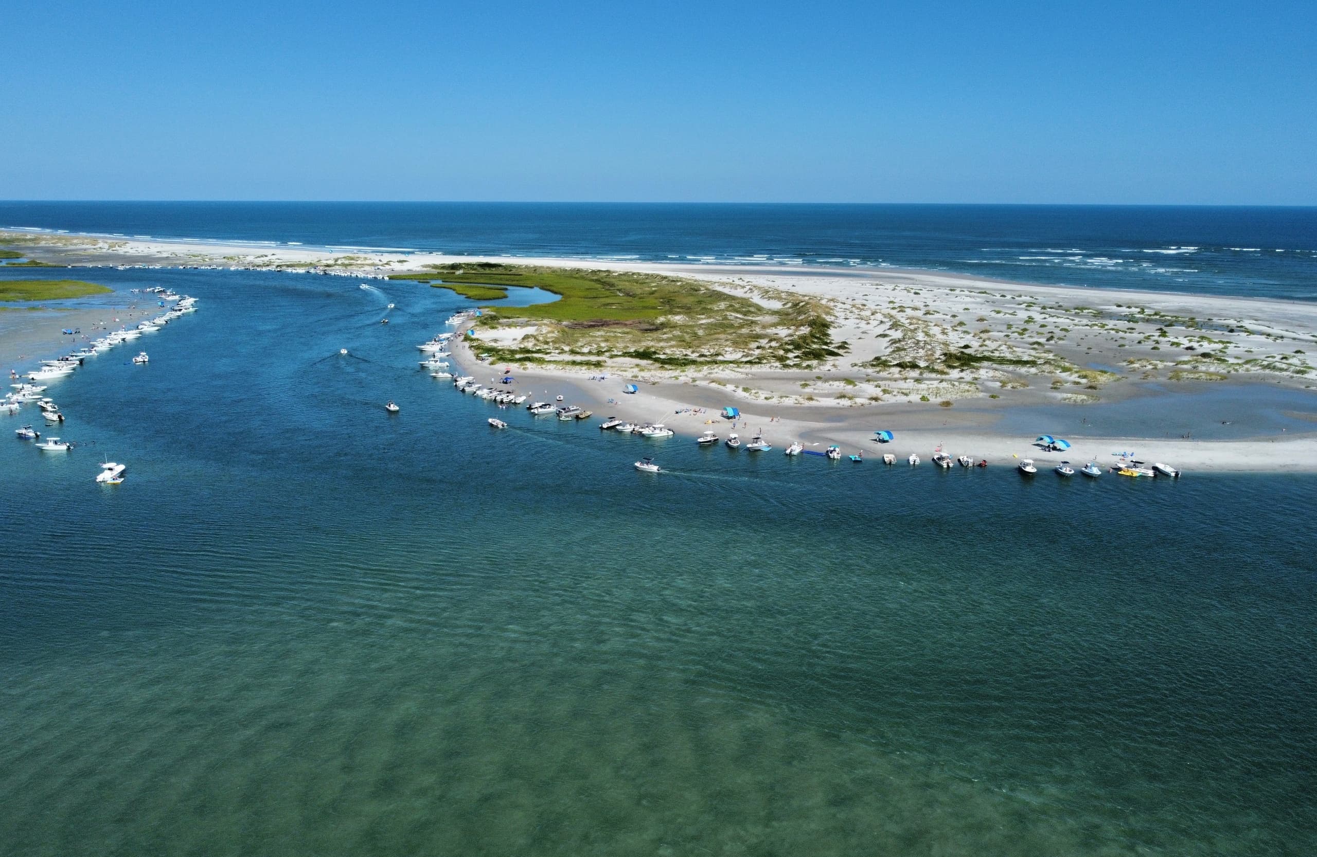 Coastal aerial of sandy spit and tidal marshes under blue sky