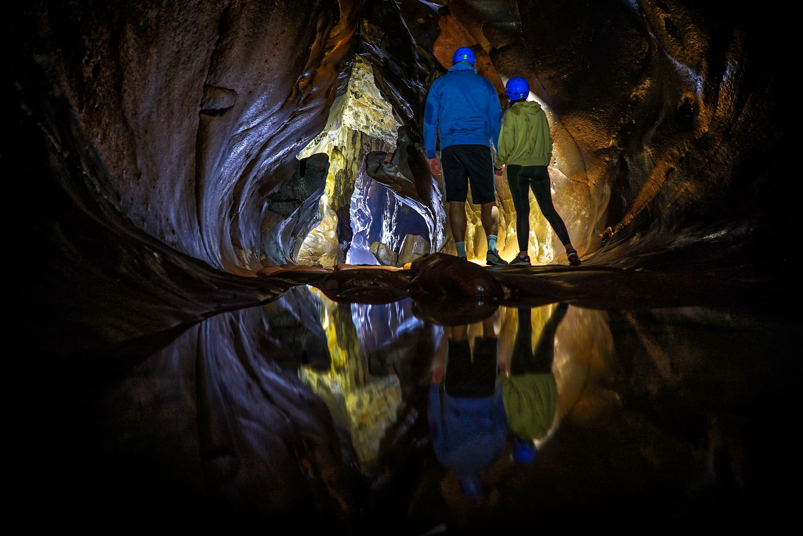 Cave explorers with helmets reflected in subterranean pool