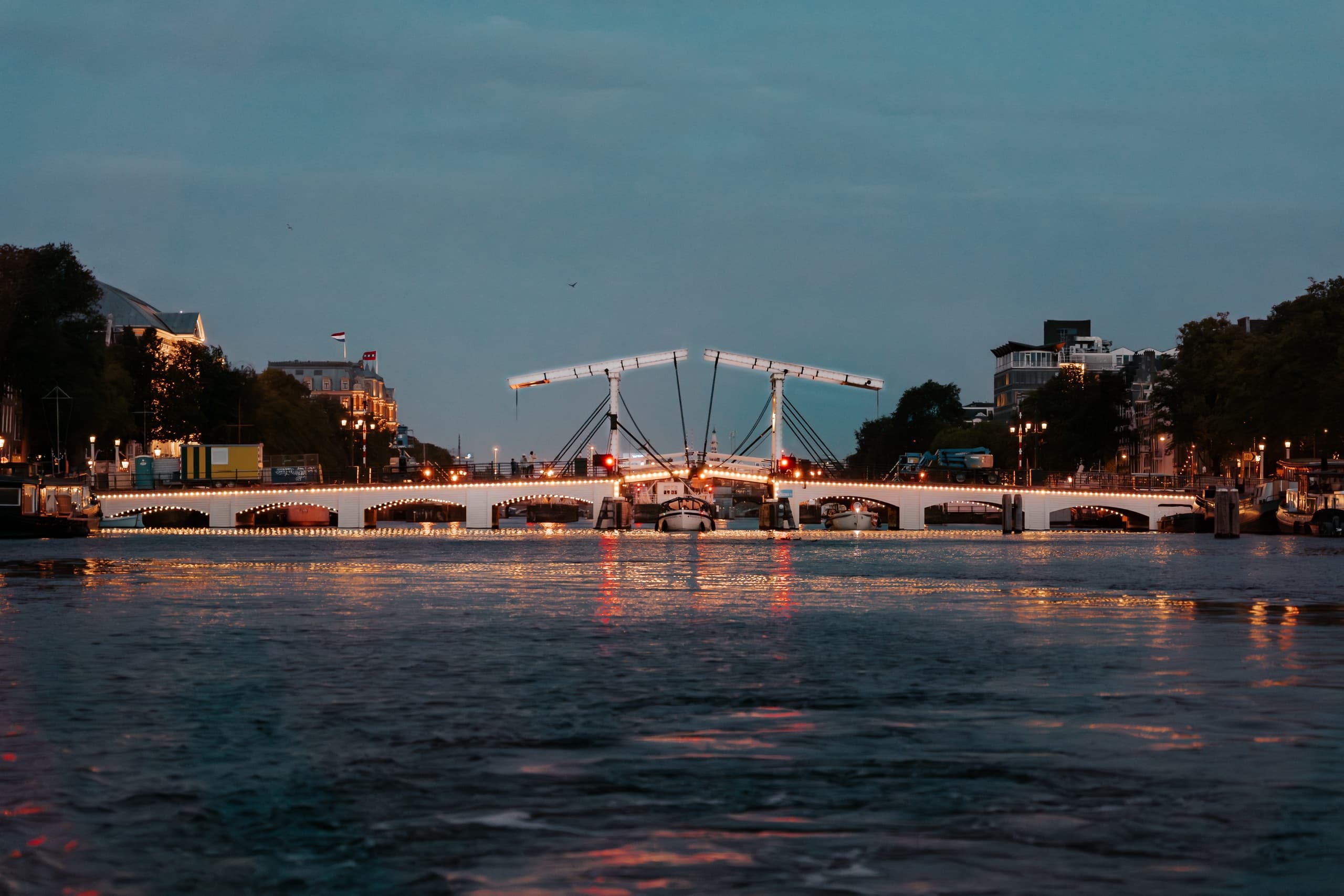 Illuminated bridge and city lights over Amsterdam canal at dusk