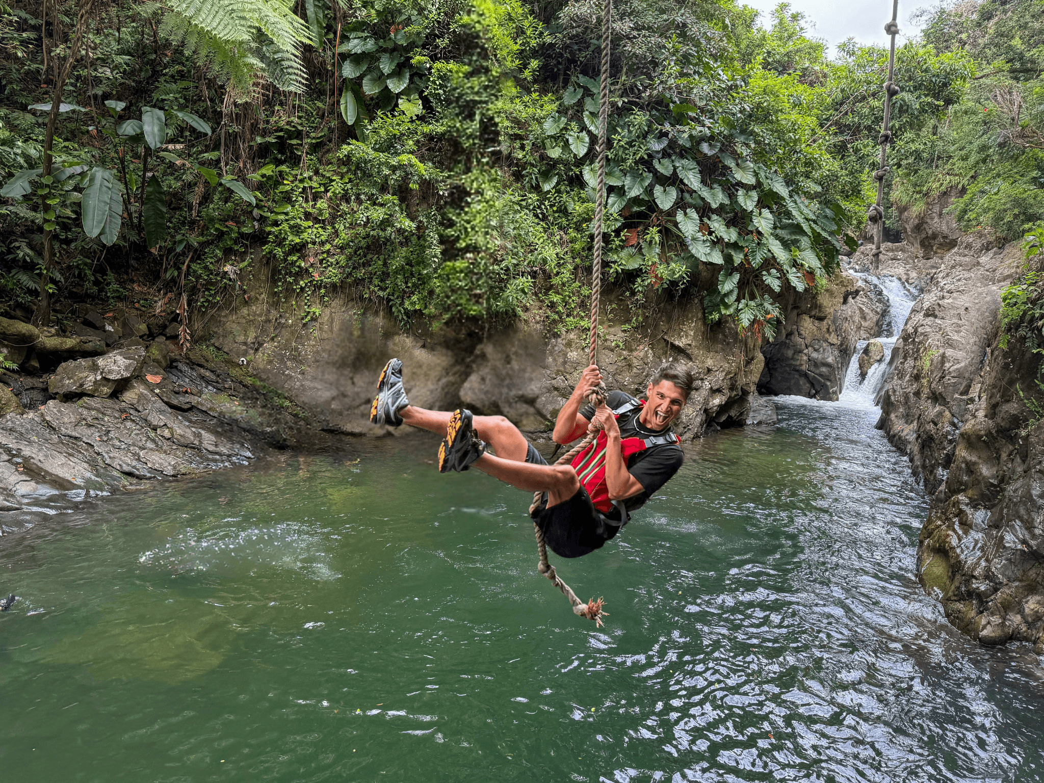 Rope swinging over jungle pool in tropical canyon