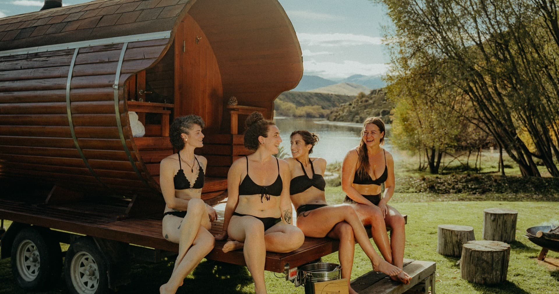 Group relaxing outside barrel sauna with lake and mountain view