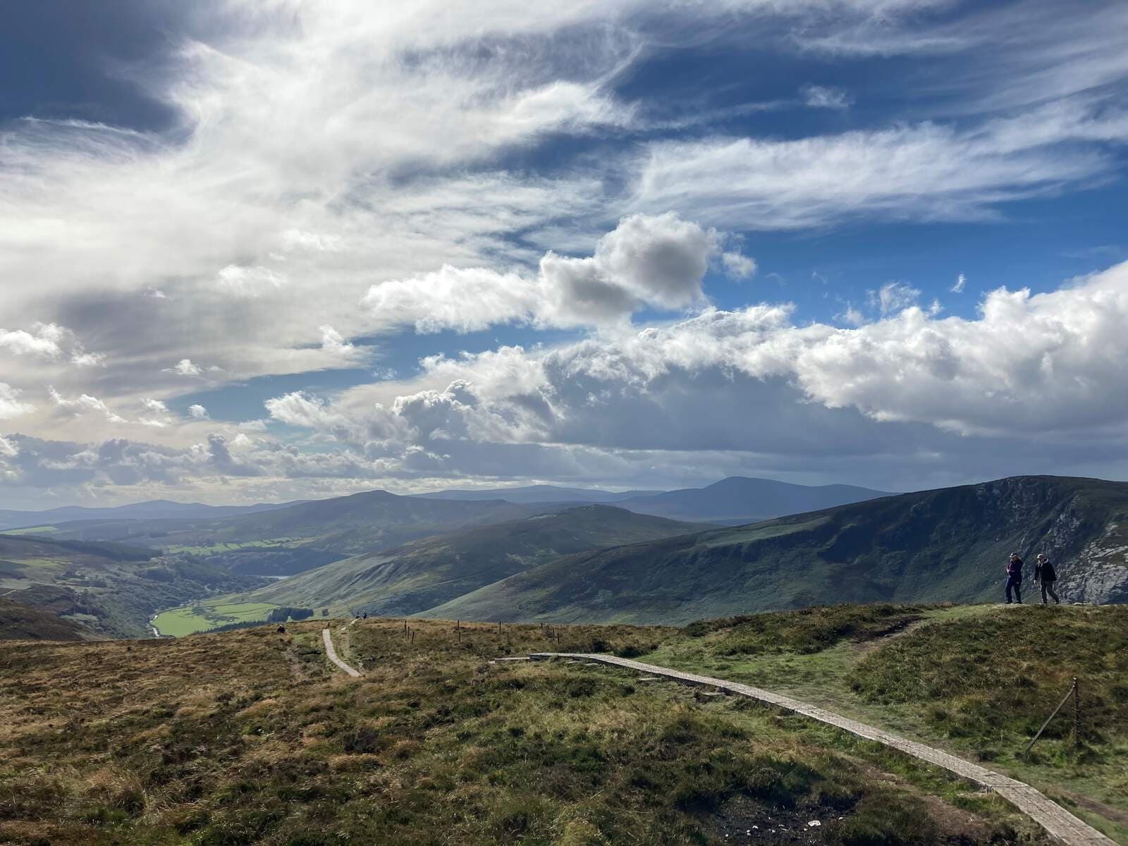 Hikers on ridge trail amid mountain vista under dramatic clouds