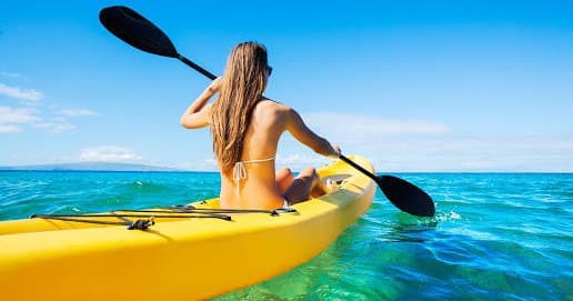 Solo kayaker paddling bright yellow kayak on clear turquoise sea