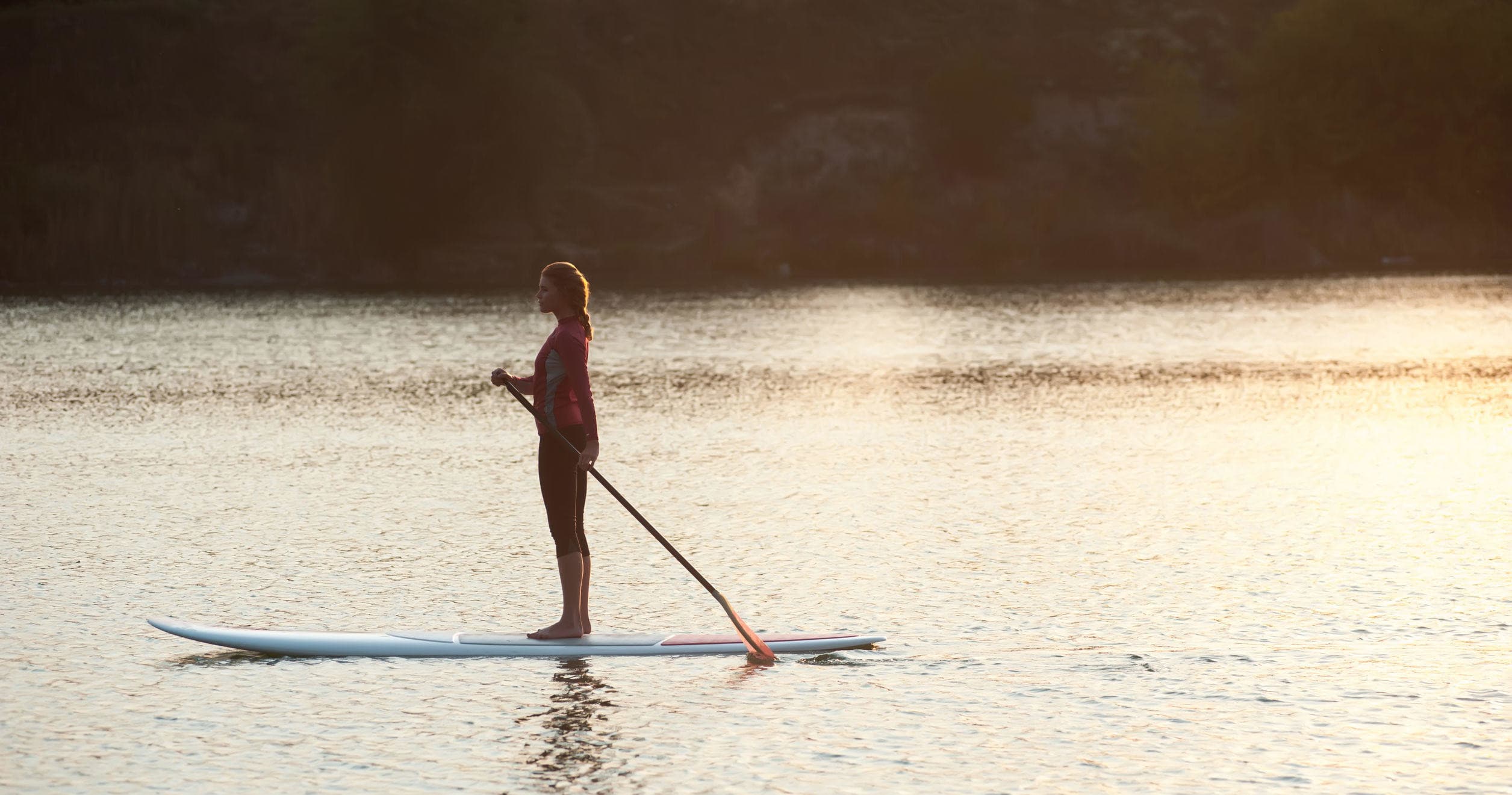 Stand-up paddleboarder at sunset on calm lake with orange sky glow