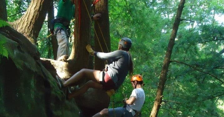 Rock climbers navigating forested sandstone cliffs in Hocking Hills