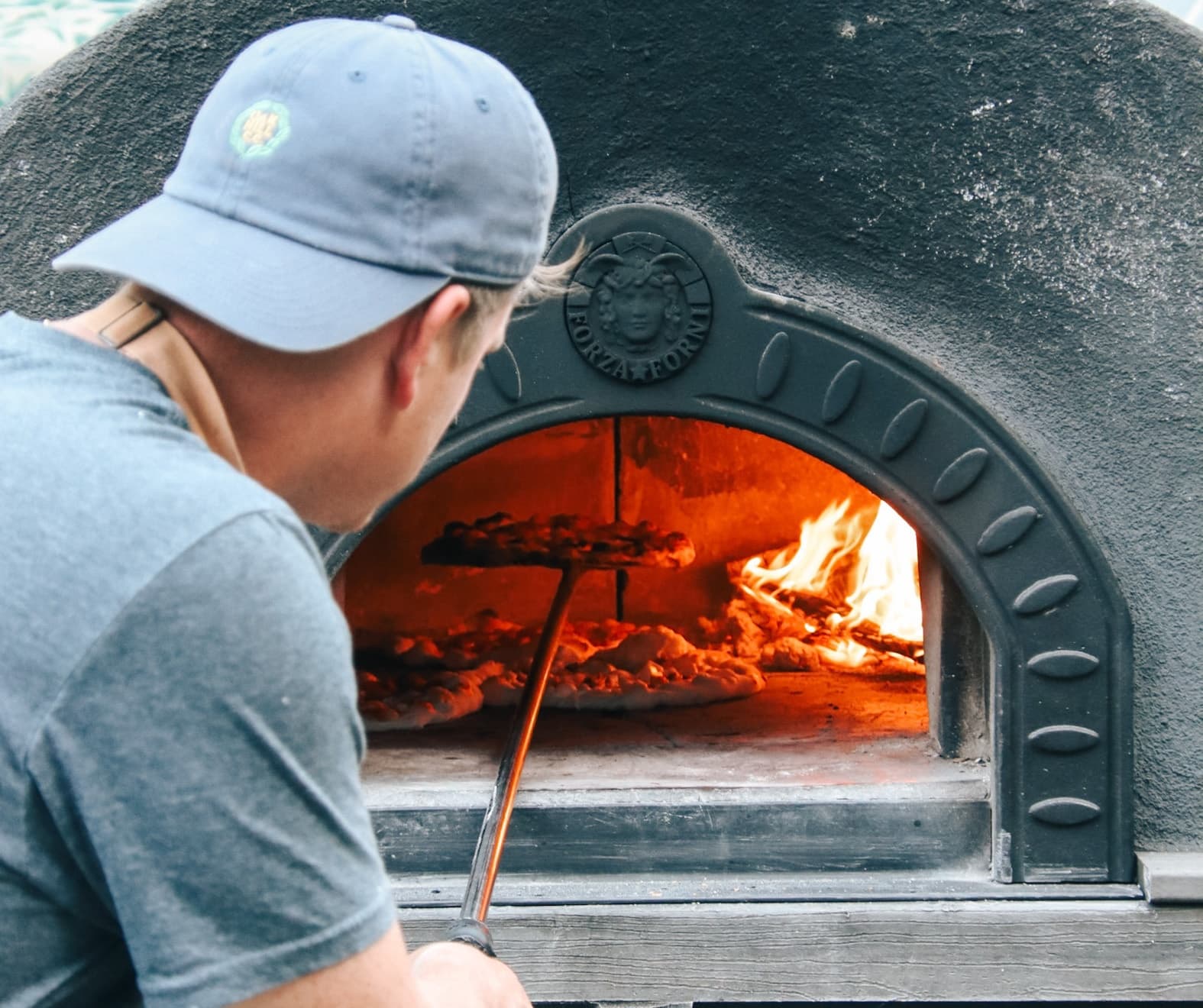 Baker tending wood-fired oven for artisanal pizza at winery