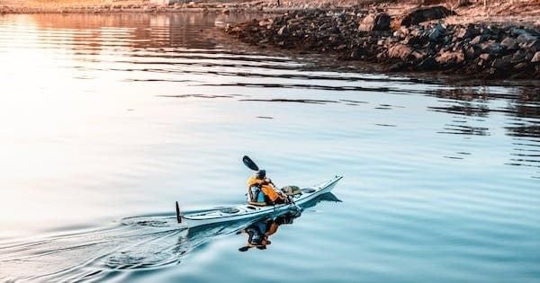 Solo kayaker paddling on calm reflective coastal inlet