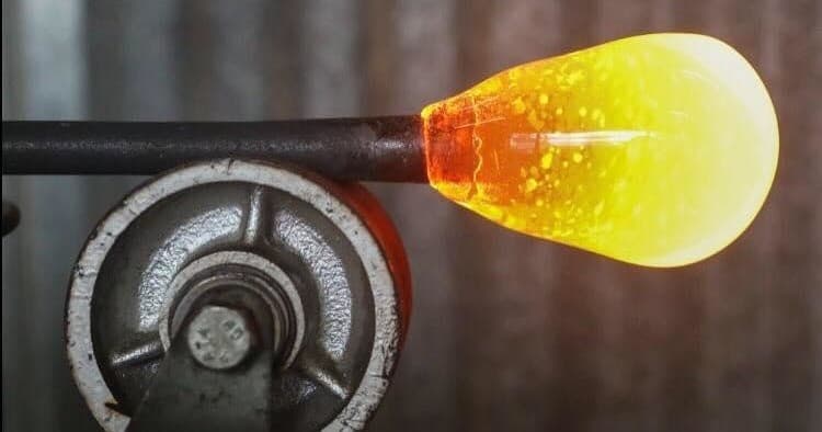 Hot glass gather on rod glowing in glass studio furnace