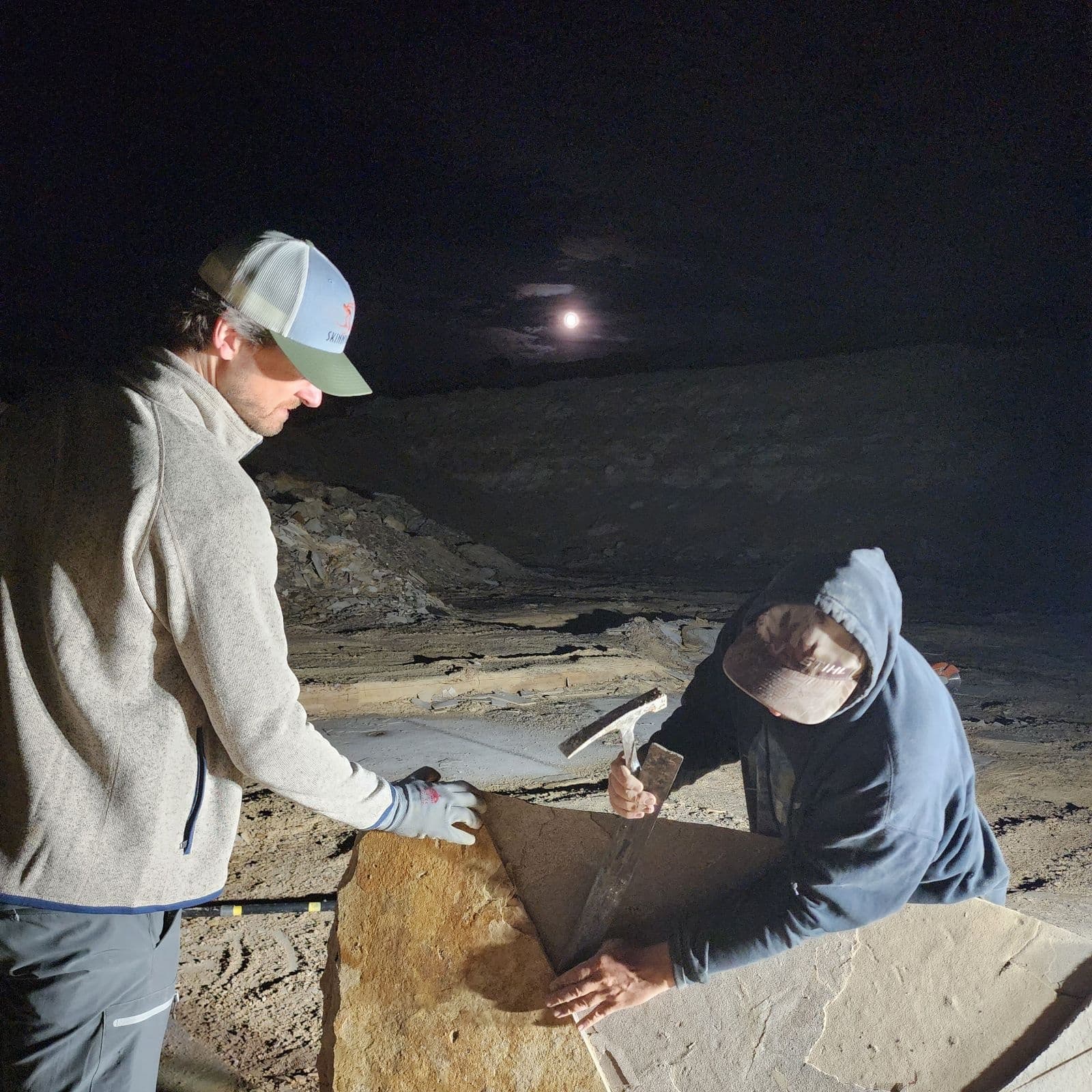 Nighttime fossil excavation under moonlight on desert outcrop