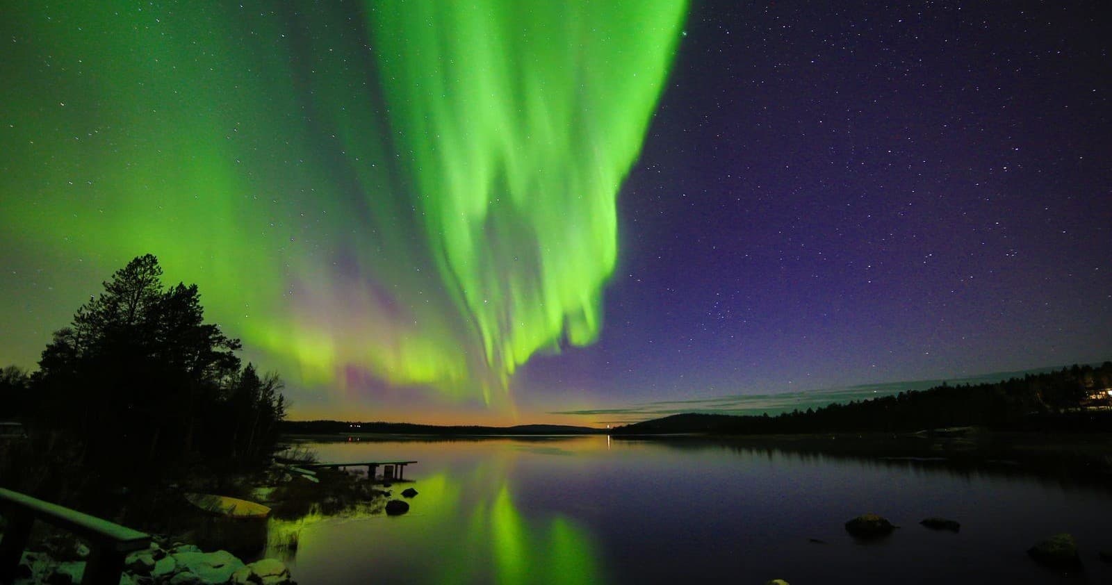 Vivid aurora reflecting on lake at dusk in Finnish Lapland