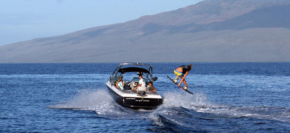 Wakeboarder jumping behind boat off Maui coastline in ocean