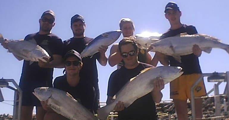 Fishing crew posing with multiple catches on sunny boat
