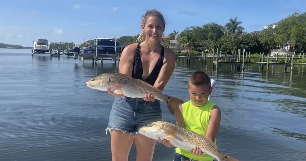 Mother and son holding fish on boat in calm coastal inlet
