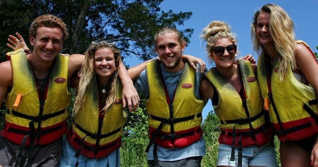 Smiling paddlers in life jackets posing outdoors at riverbank