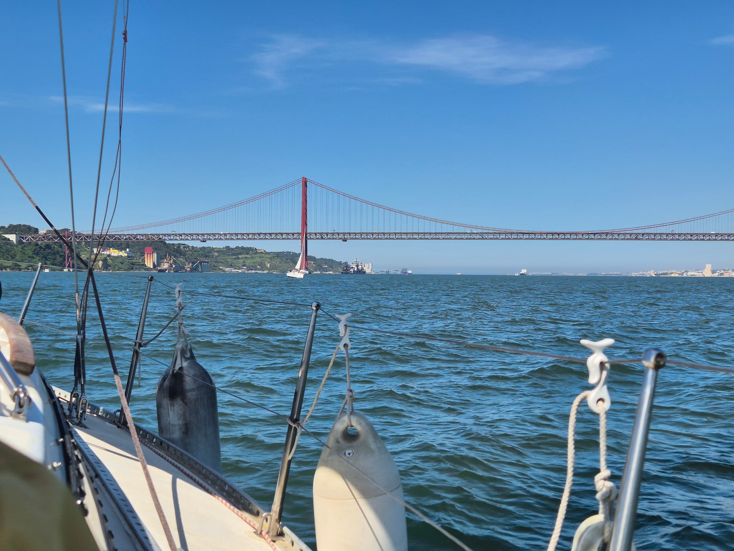 Sailboat cruising past 25 de Abril Bridge in Lisbon bay