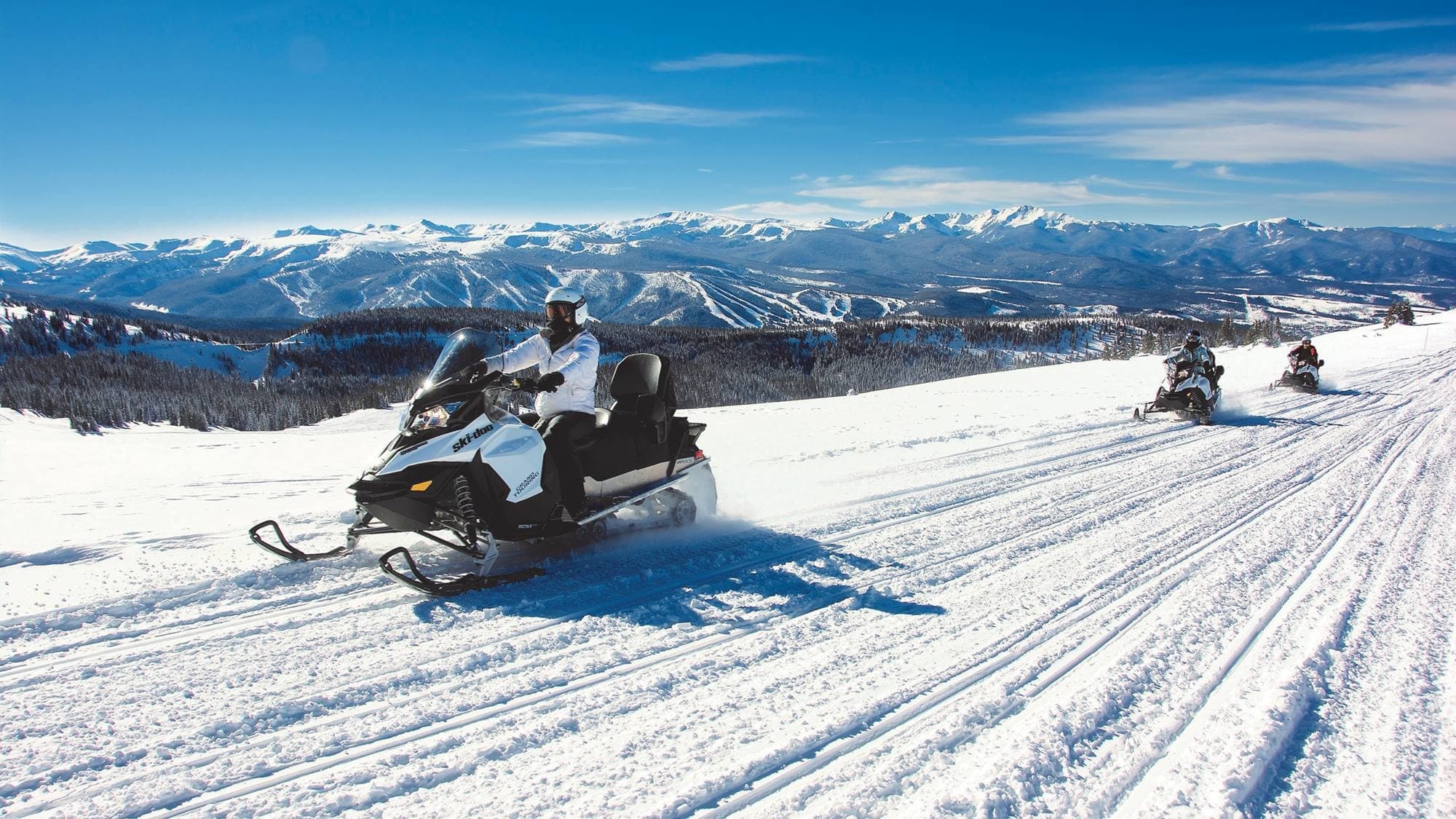 Snowmobilers racing on groomed mountain trail with vistas