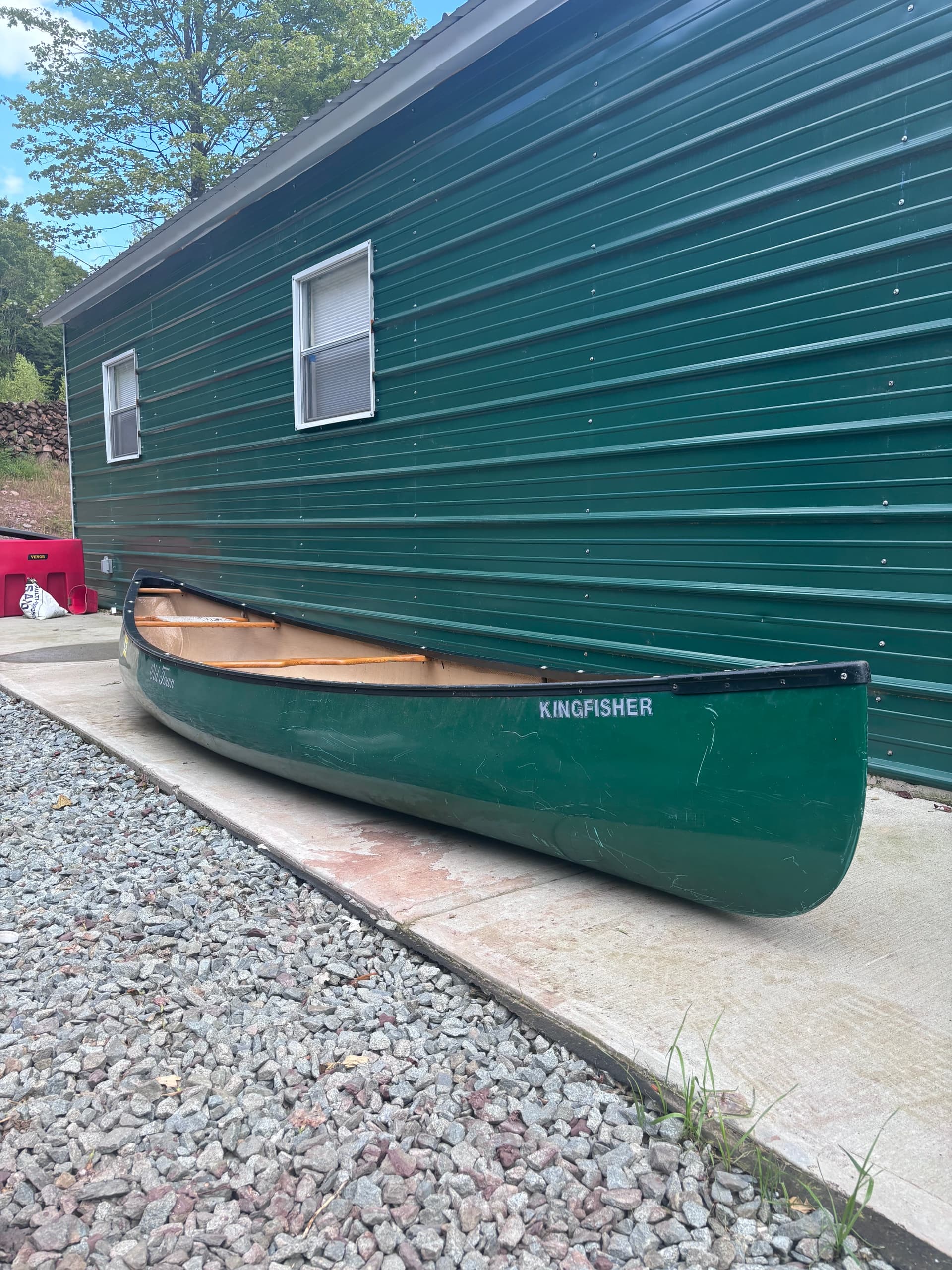 Green canoe beside cabin on gravel pad, ready for paddling