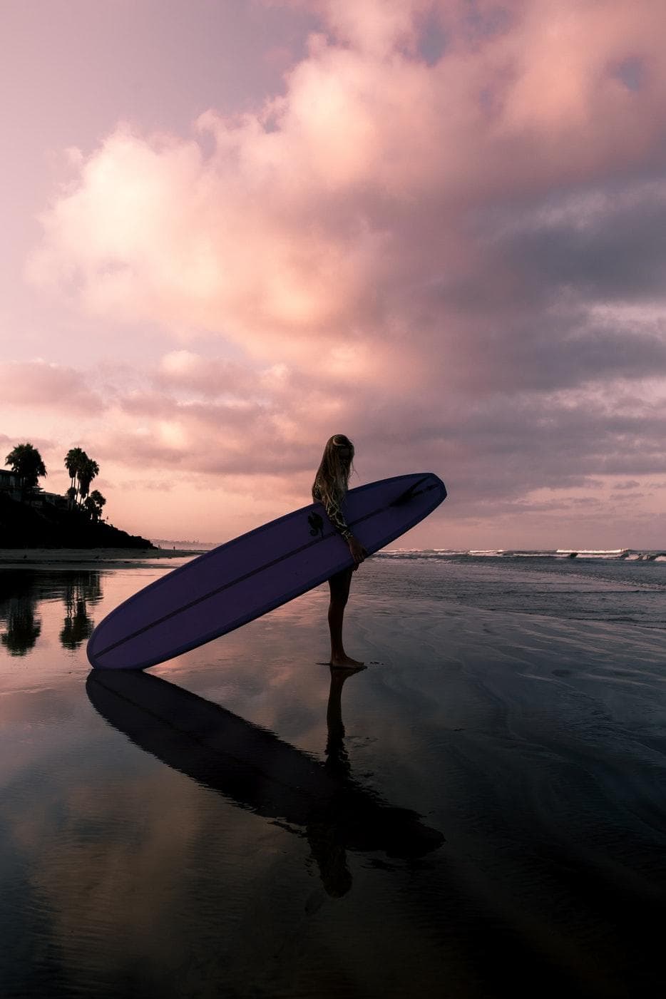 Surfer with board at Kauai sunset, reflection on wet sand