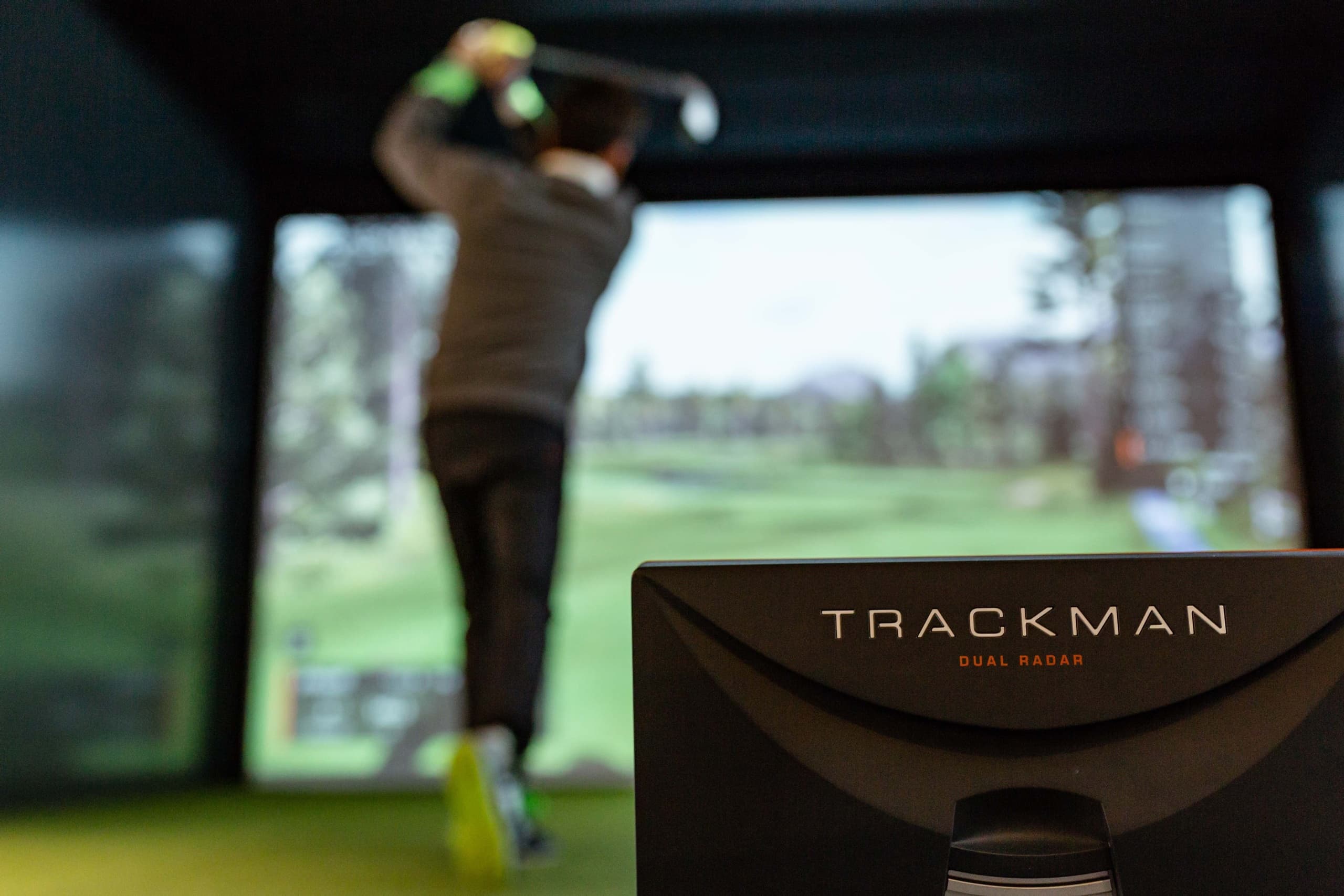 Blurred golfer swing with TrackMan monitor in indoor sim setting