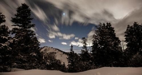 Mountain vista with dramatic long-exposure sky over snowy pines
