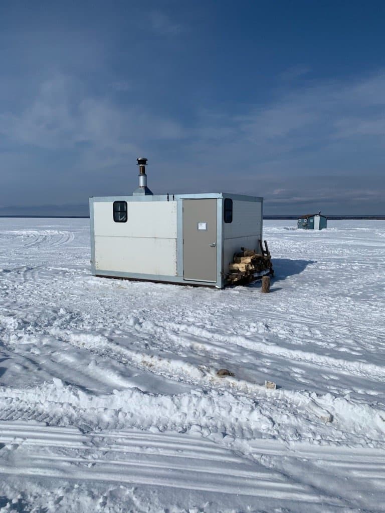Portable ice fishing shack on snowy flat lake with clear sky