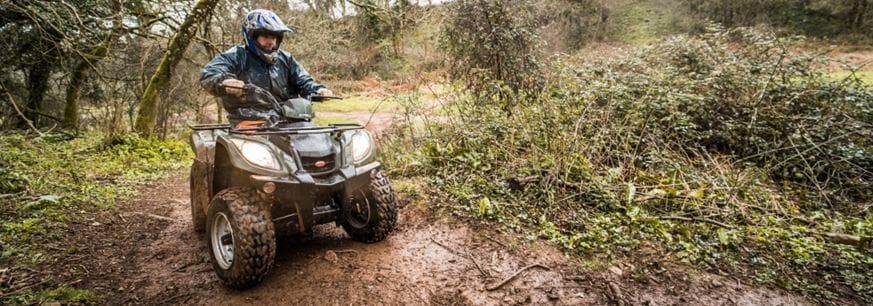 Single ATV riding through muddy forest trail in woodland
