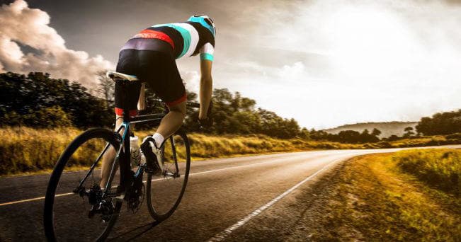 Road cyclist riding into sunrise on a scenic country road