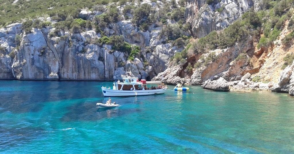 Boat anchored in turquoise coastal cove by rocky cliffs