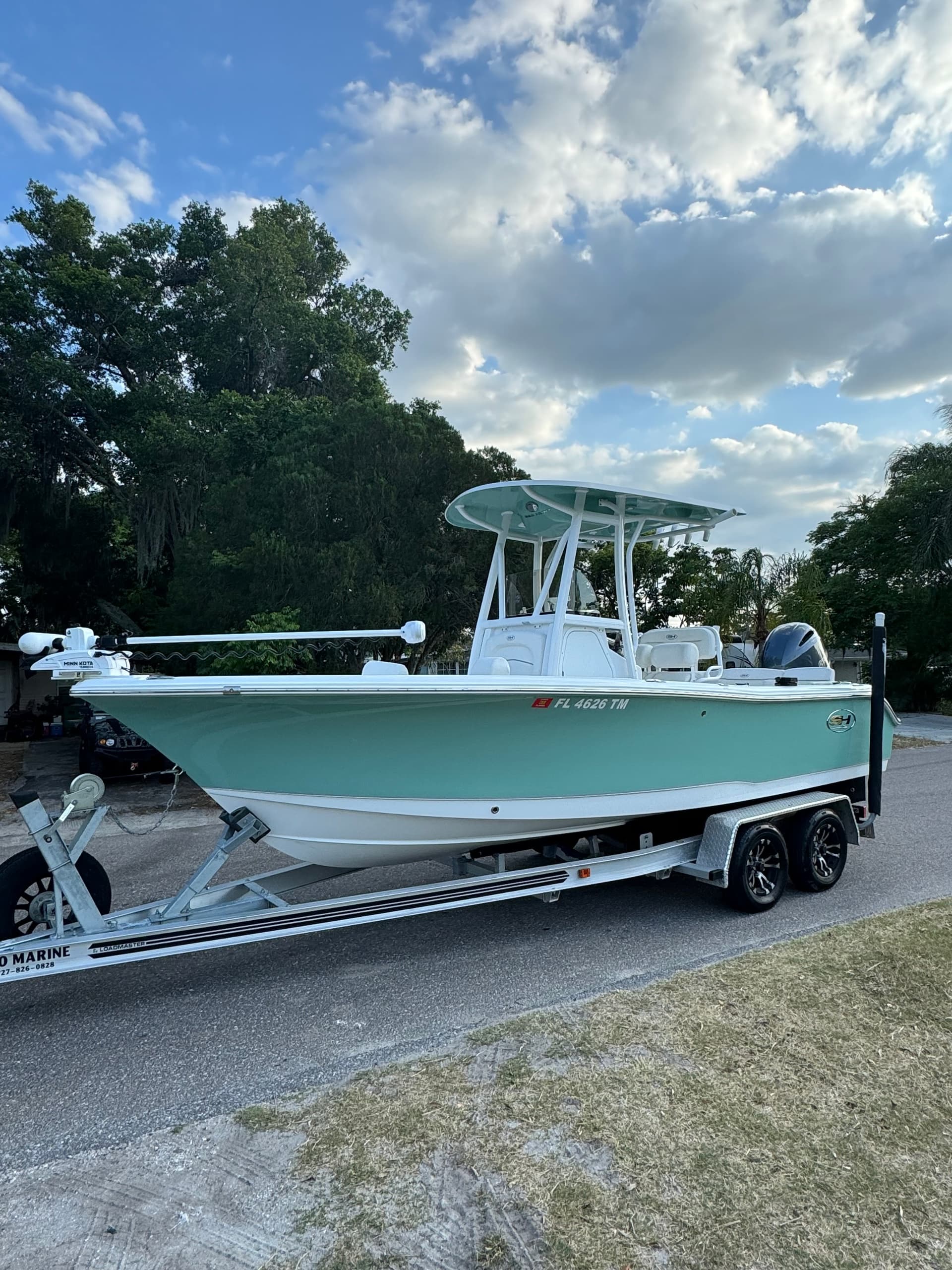 Center console fishing boat on trailer parked near coastal trees
