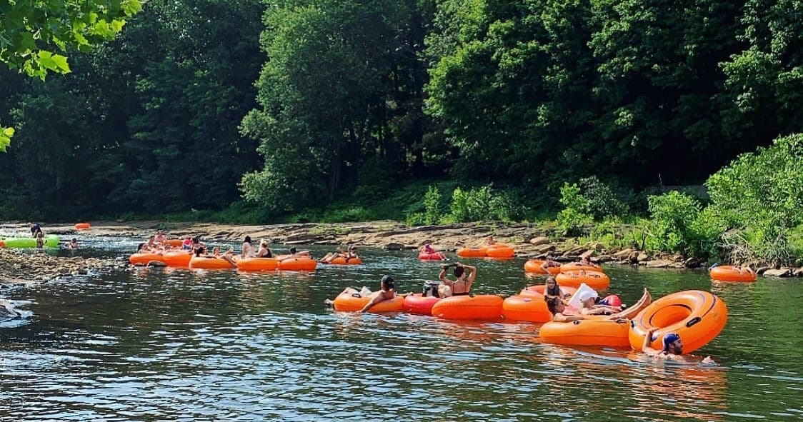 Tubers floating down forested river on orange inner tubes