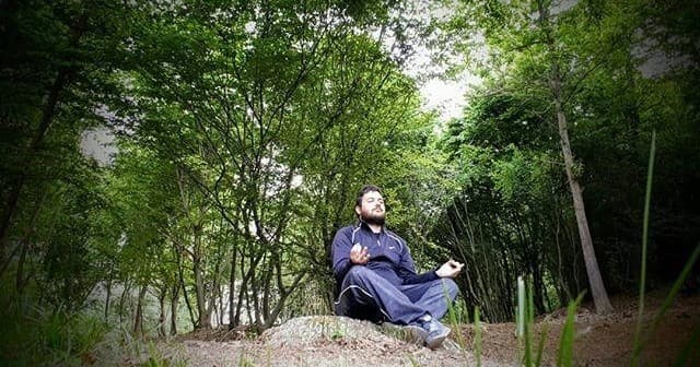 Person meditating on forest rock amid trees, peaceful outdoor retreat