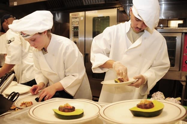 Culinary students plating dishes in busy restaurant kitchen service
