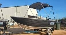 Black tinny boat with bimini on trailer parked near harbor shed