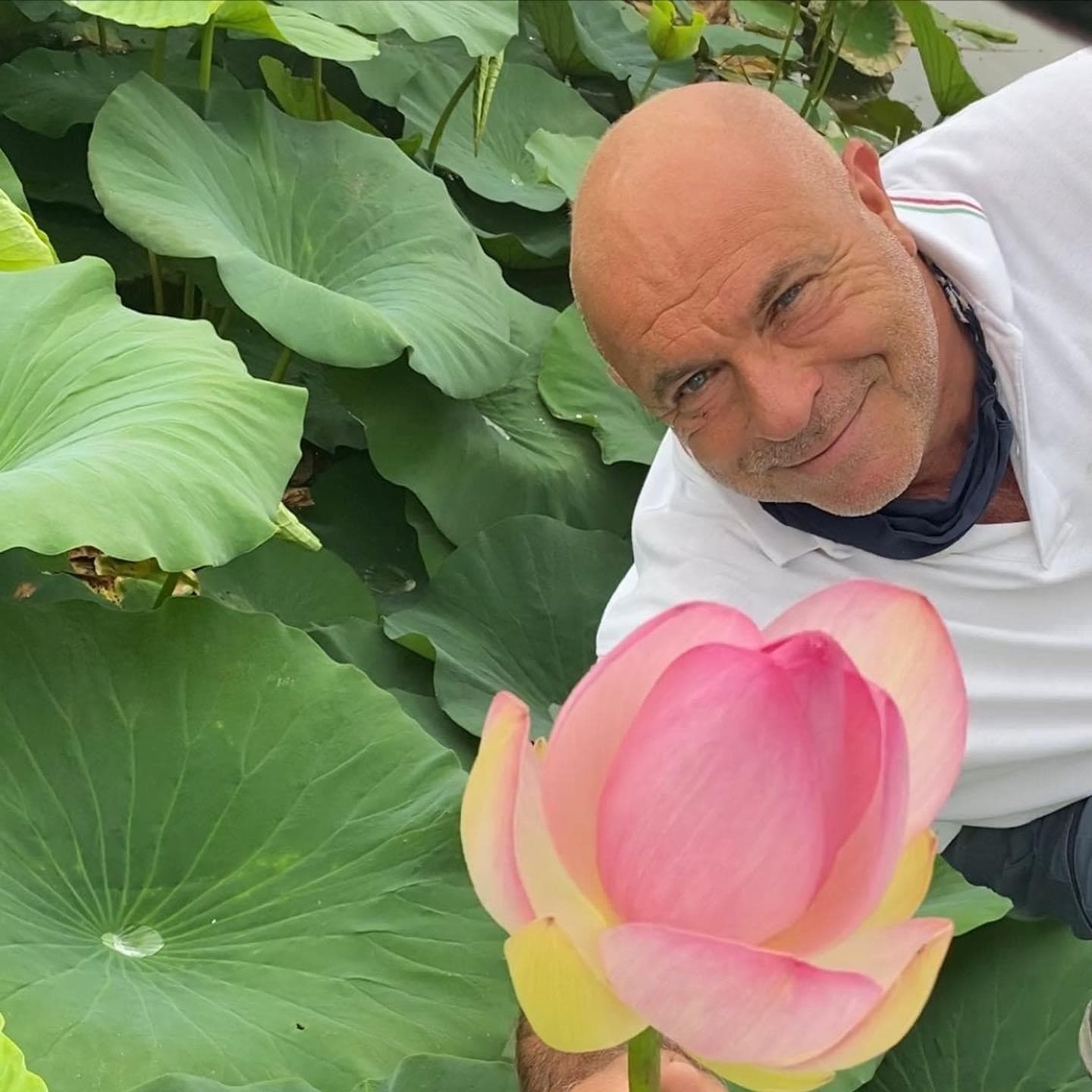 Visitor smiling beside pink lotus flower in pond habitat