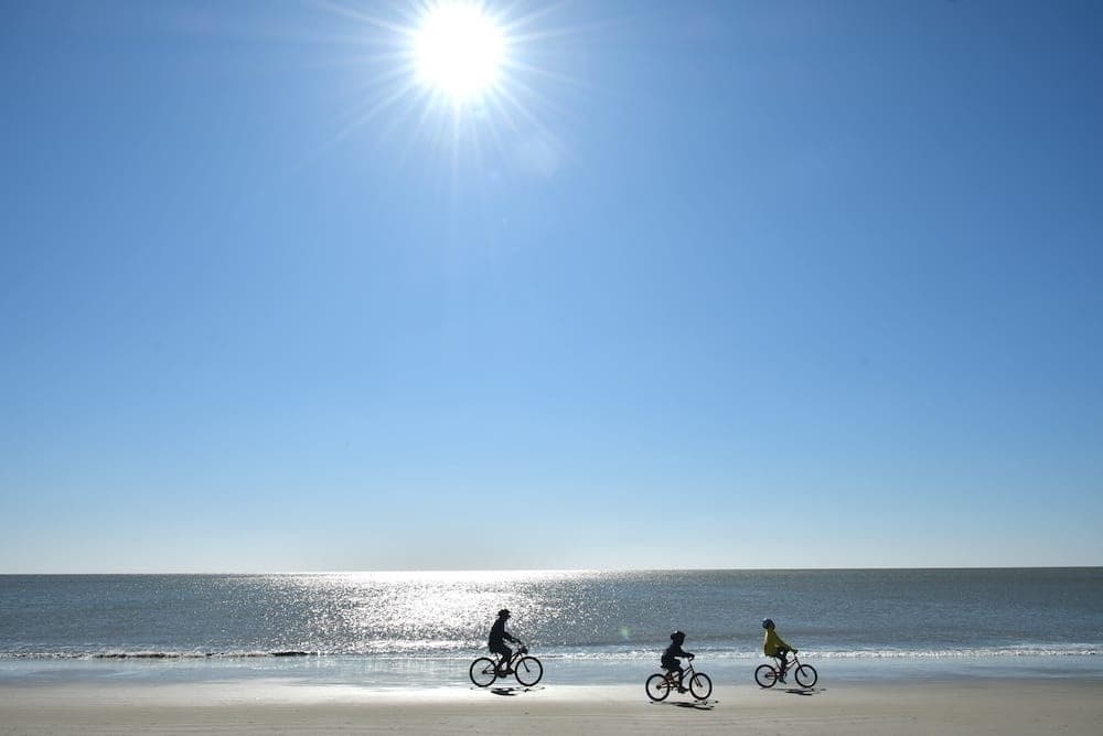 Three cyclists silhouetted against bright sun on coastal beach