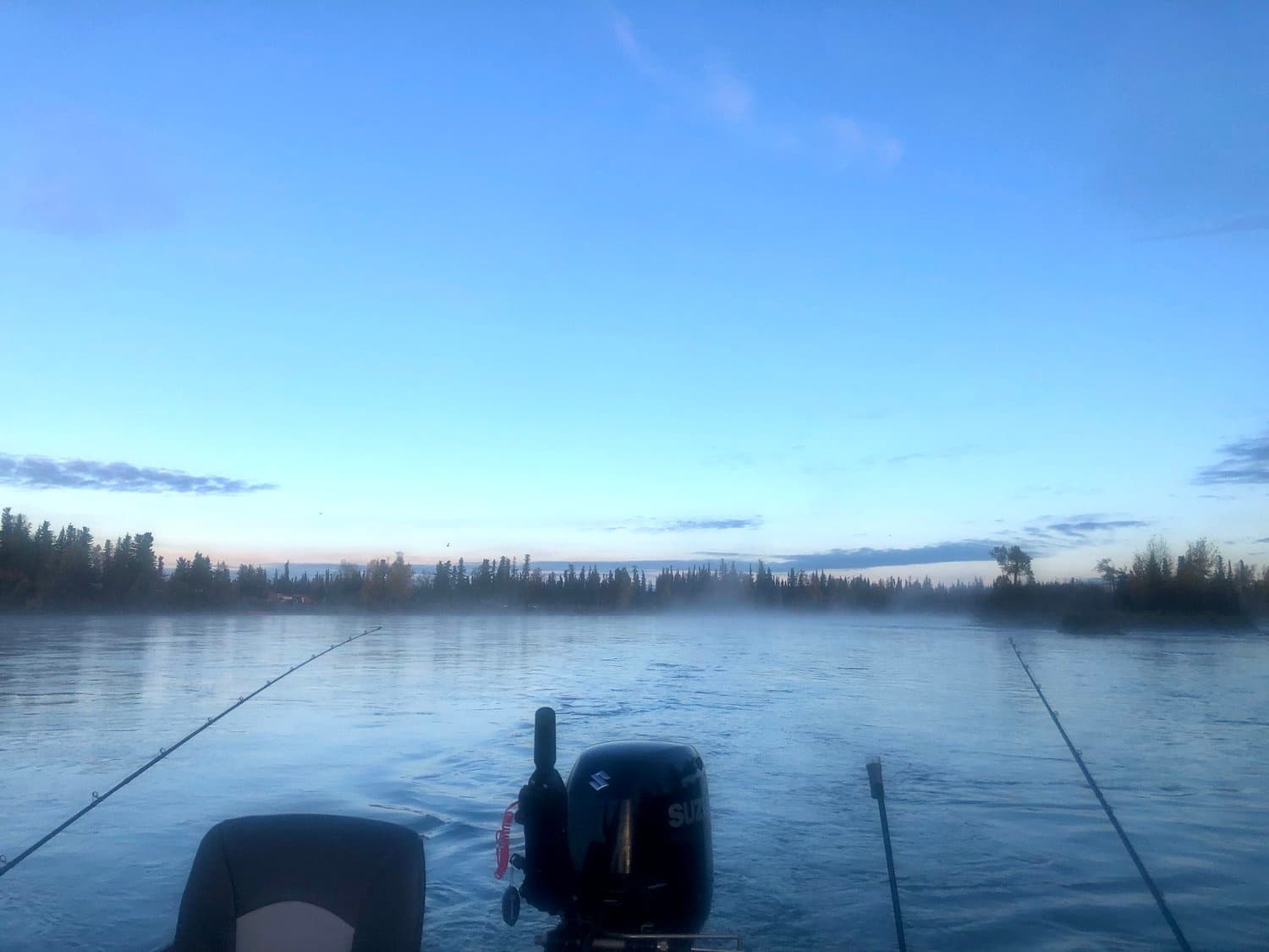 Fishing charter boat on calm Kenai River at dawn with rods
