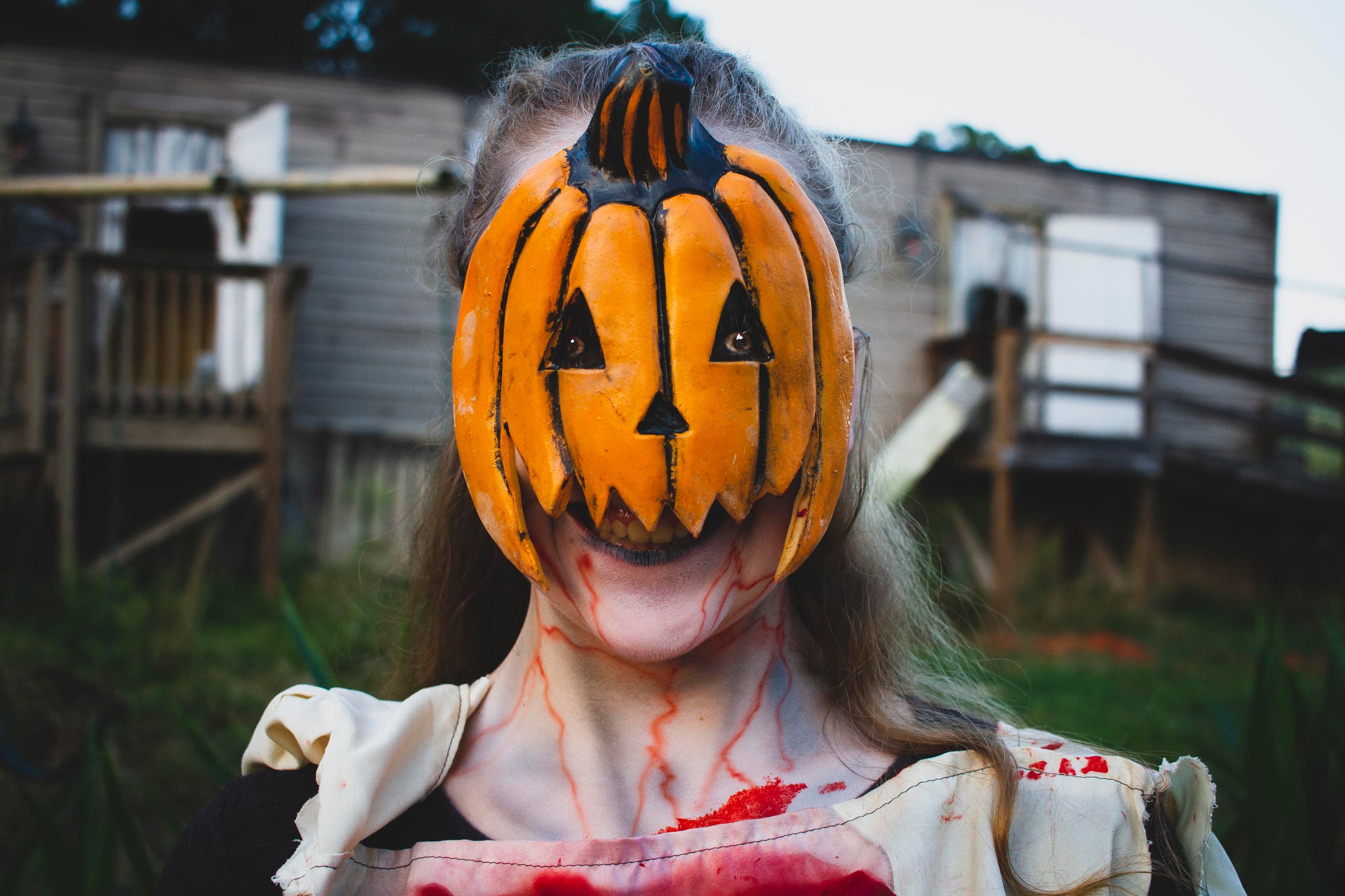 Pumpkin-headed actor outside rural trailer haunt, blood-stained