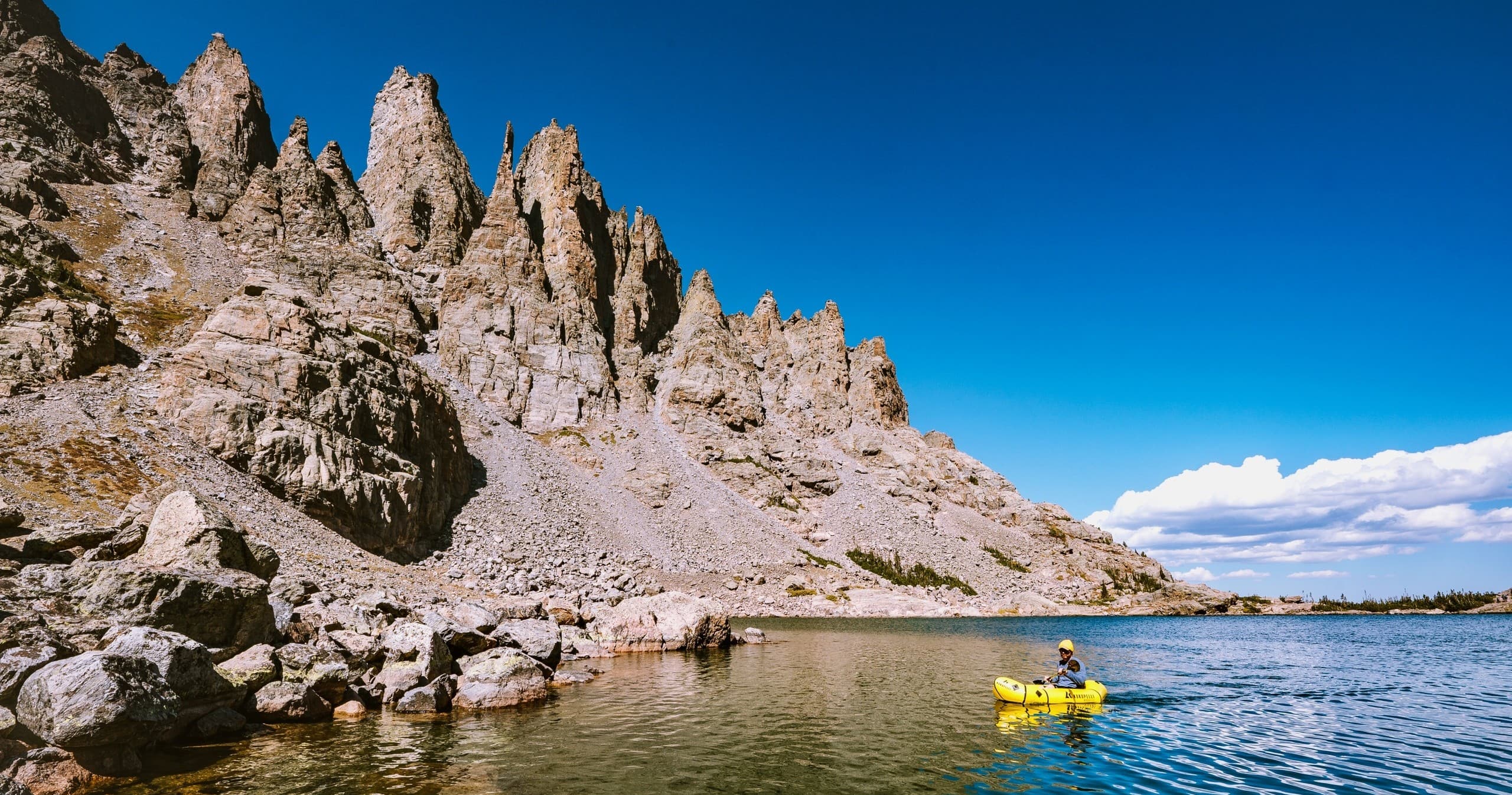 Packrafter paddling beside jagged alpine peaks on lake