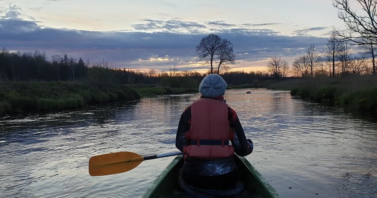 Canoeist paddling through Soomaa wetland river at sunset