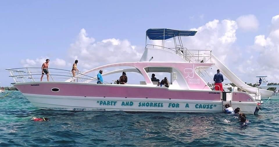 Pink party boat on open sea with guests enjoying snorkeling
