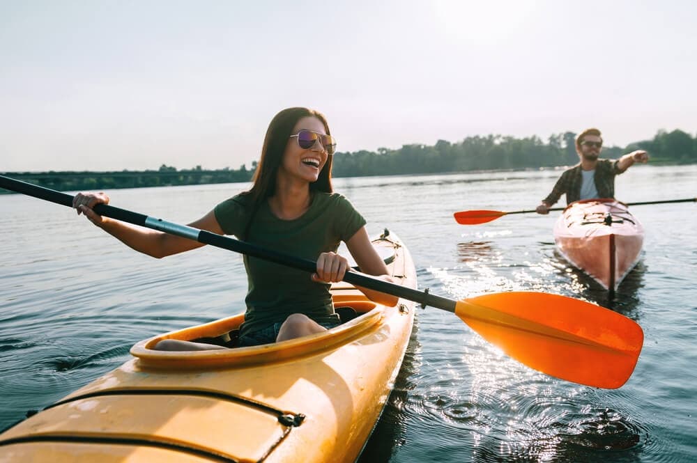 Kayakers paddling tandem kayaks on calm lake, recreational outing
