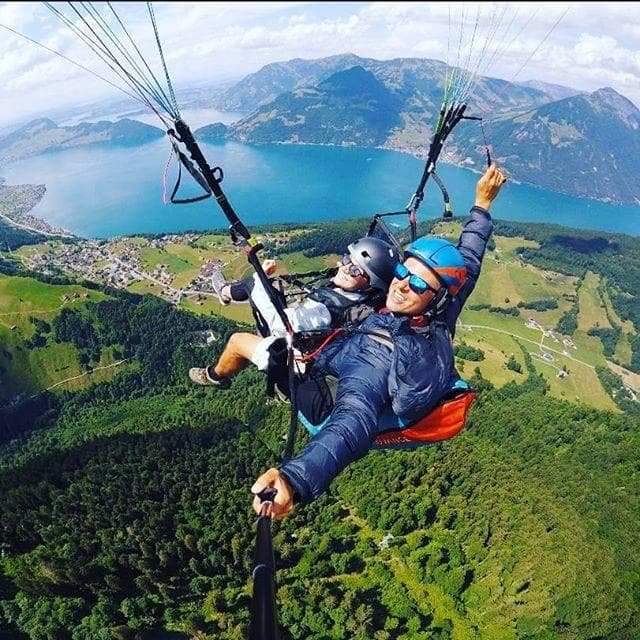 Tandem paragliders soaring above alpine lake and green valley