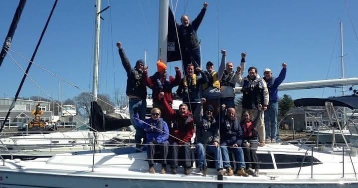 Large sailing crew cheering aboard a yacht docked in marina